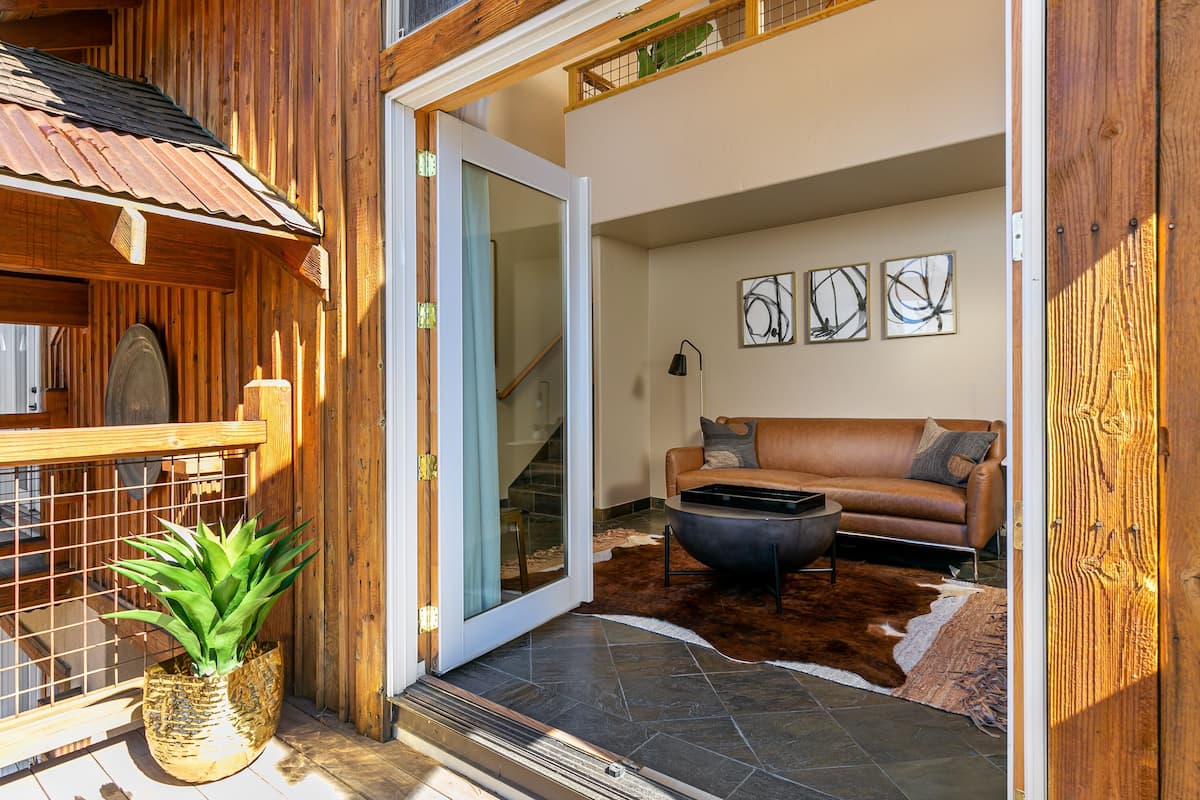 A wooden exterior with a glass door leading to an interior with a leather sofa, a fireplace, and abstract wall art.
