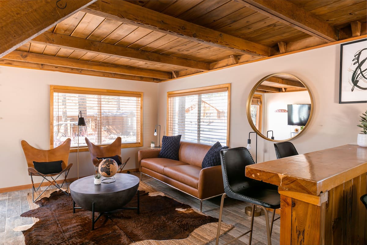 A cozy living room with a brown leather sofa, a round coffee table, and a wooden dining table.