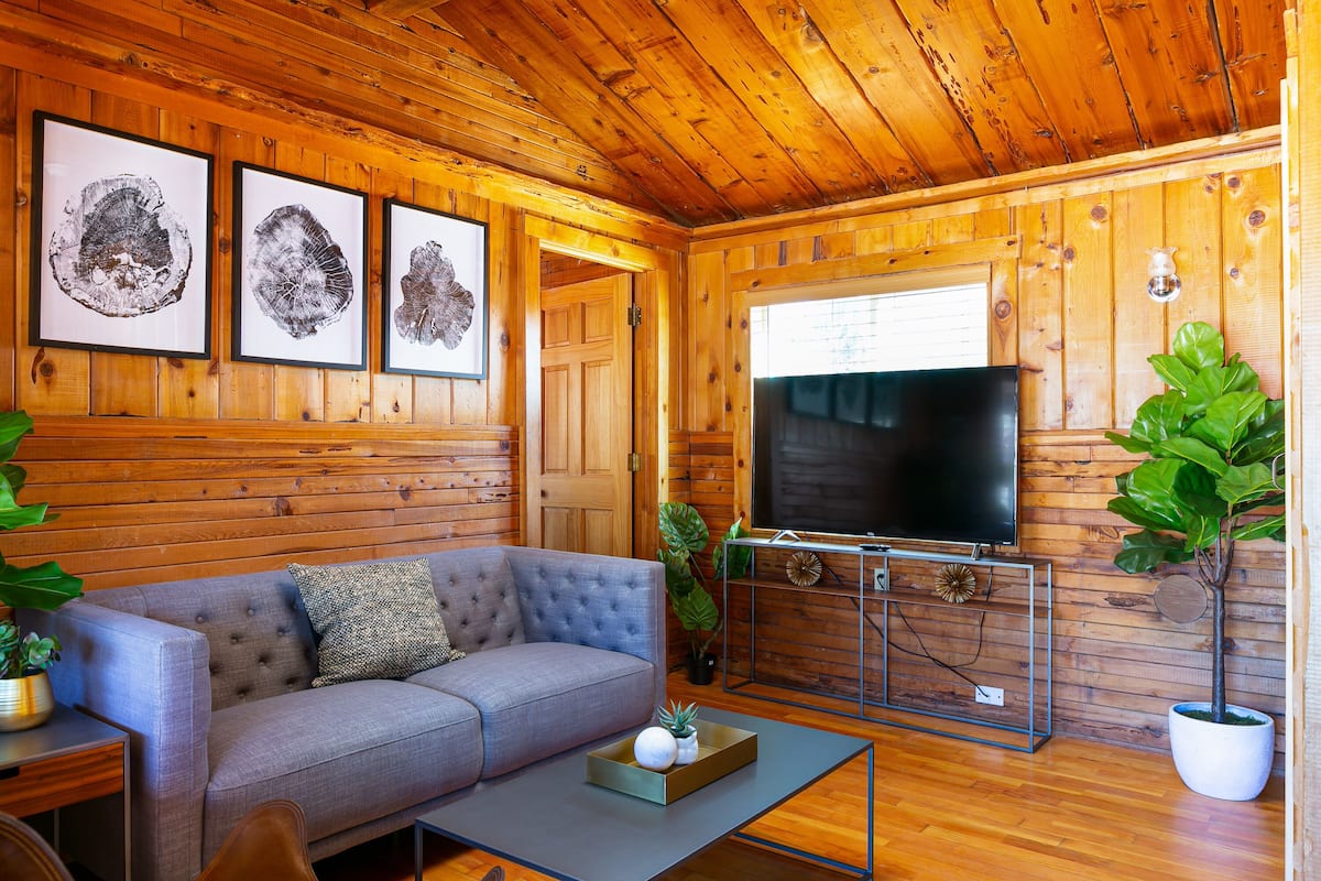 A cozy cabin interior with a wooden interior, a grey sofa, a flat-screen TV, and framed pictures on the wall.