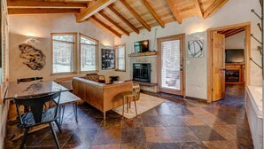 A spacious living area with a fireplace, wooden ceiling beams, and a stone-tiled floor. - Chalet View Lodge (Portola)
