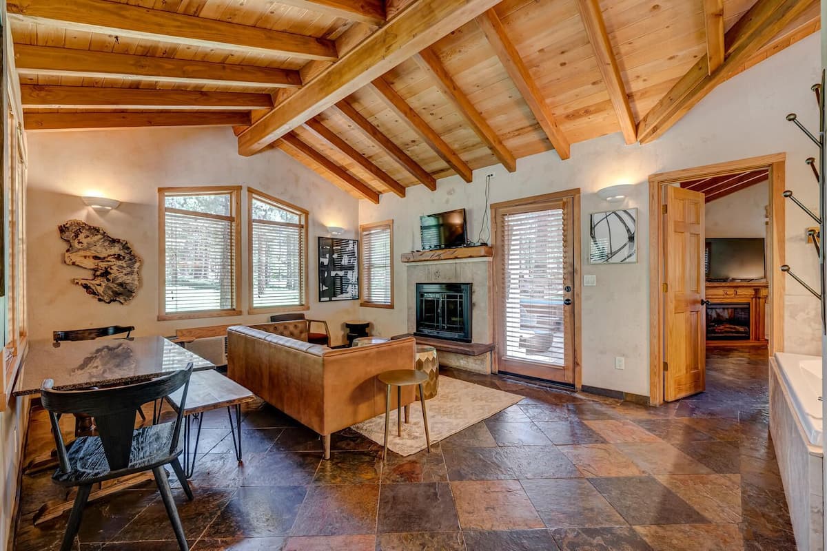 A spacious living area with a fireplace, wooden ceiling beams, and a stone-tiled floor.