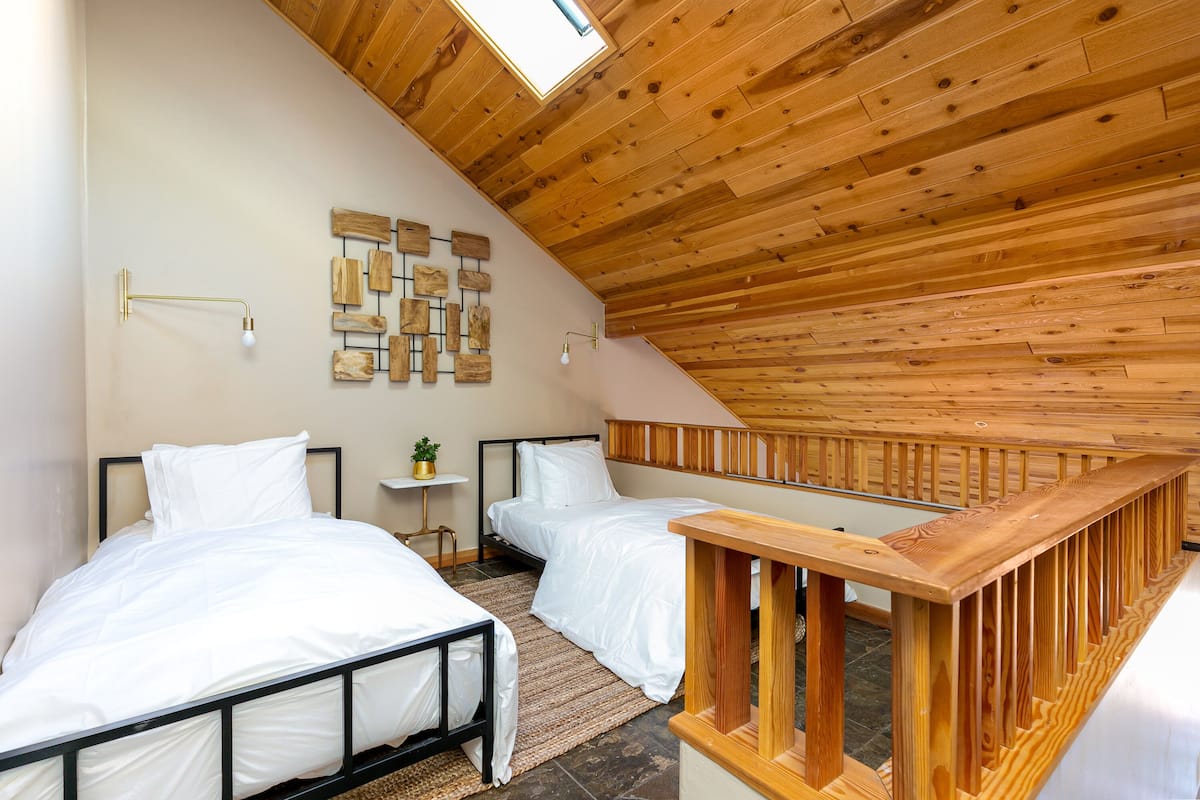 A bedroom with two beds, wooden ceiling, and a small table with a plant.