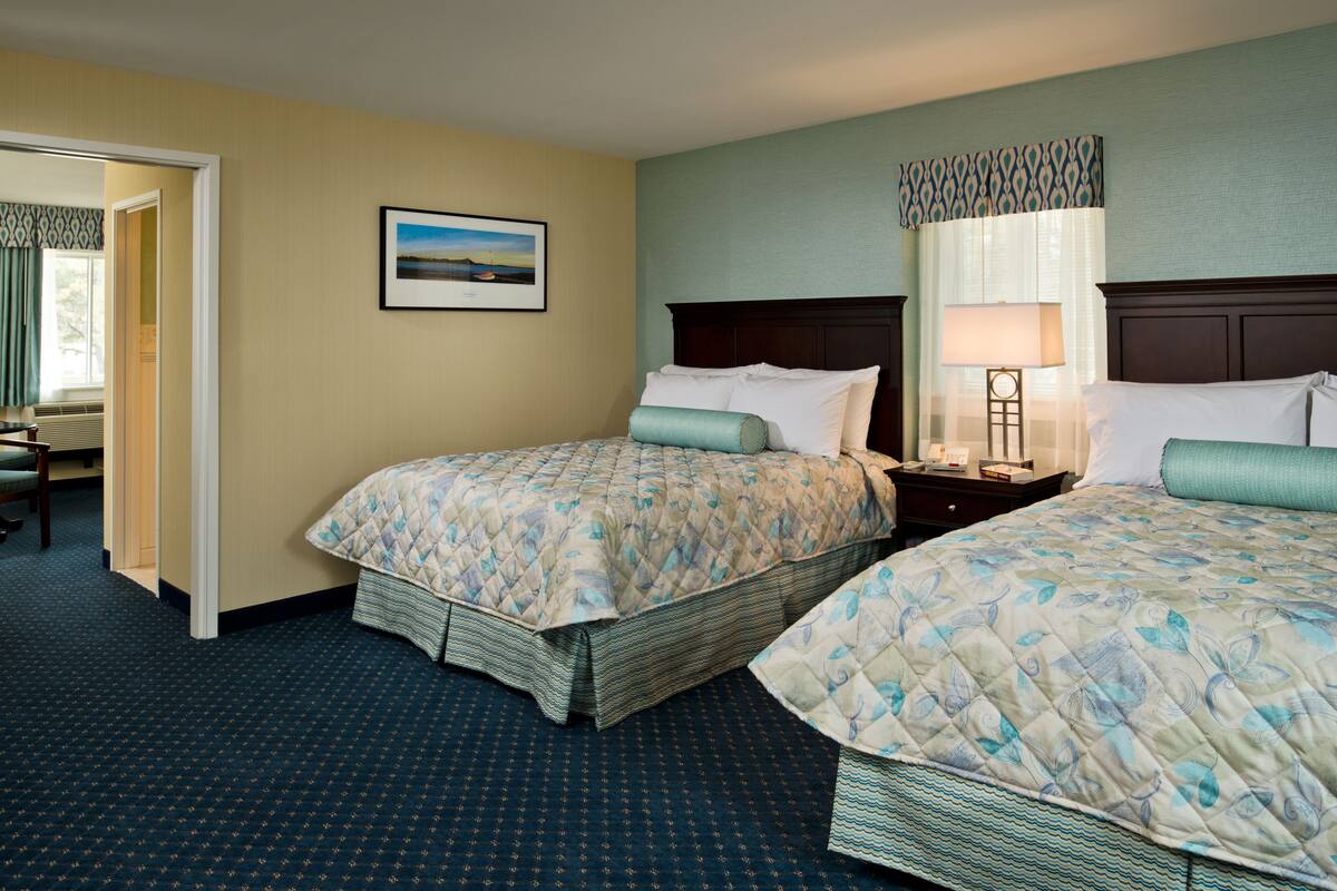 A hotel room with two beds, a nightstand, a lamp, and a framed picture on the wall.