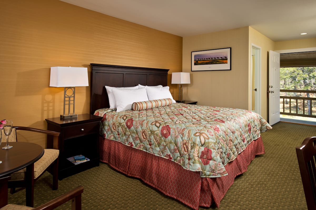 A hotel room with a large bed, two bedside tables, a chair, a small table with a glass, and a door leading to a balcony.