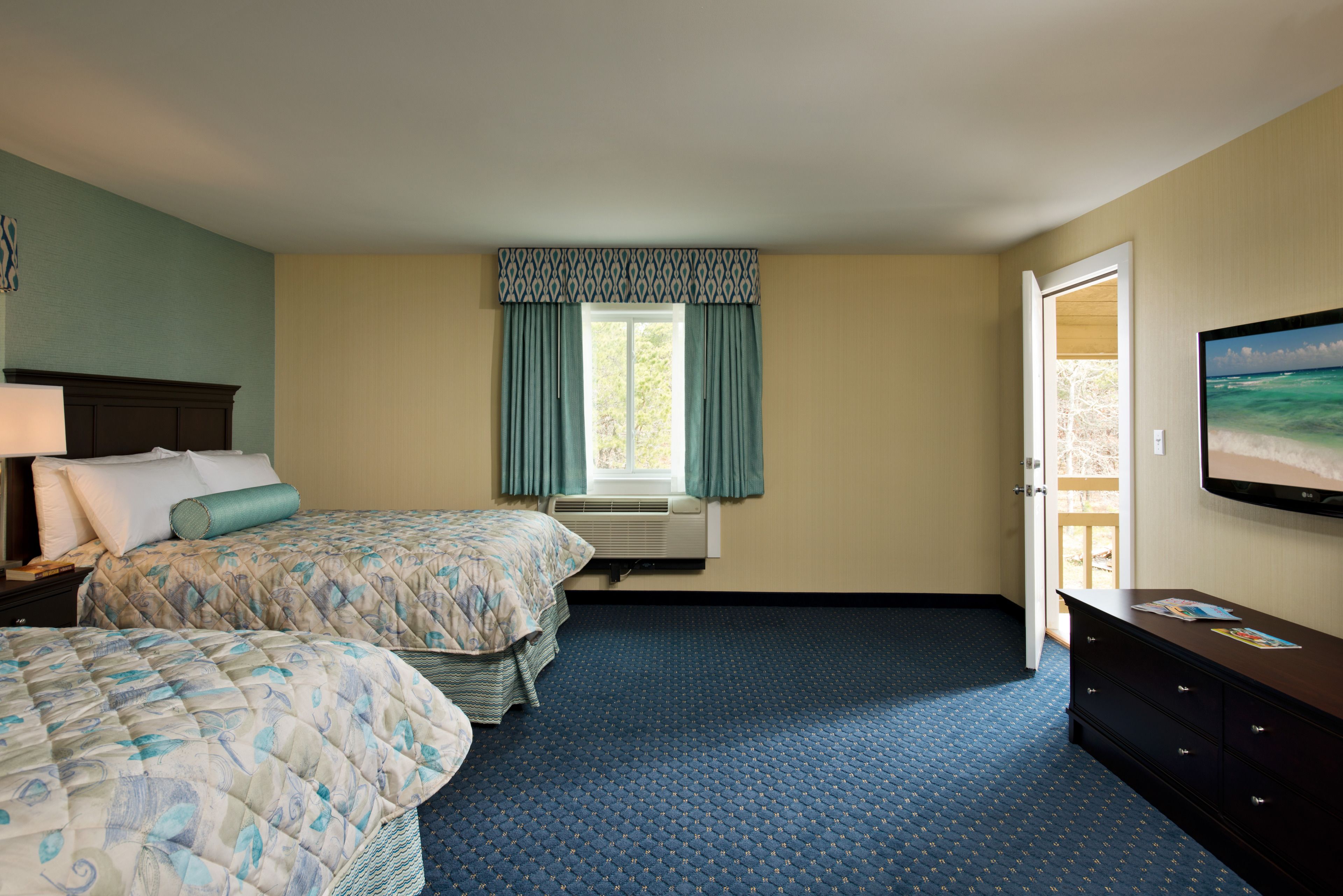A hotel room with two beds, a large window with curtains, a flat-screen TV, and a dresser.
