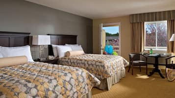 A hotel room with two beds, a desk, a chair, and a window with a view of trees.