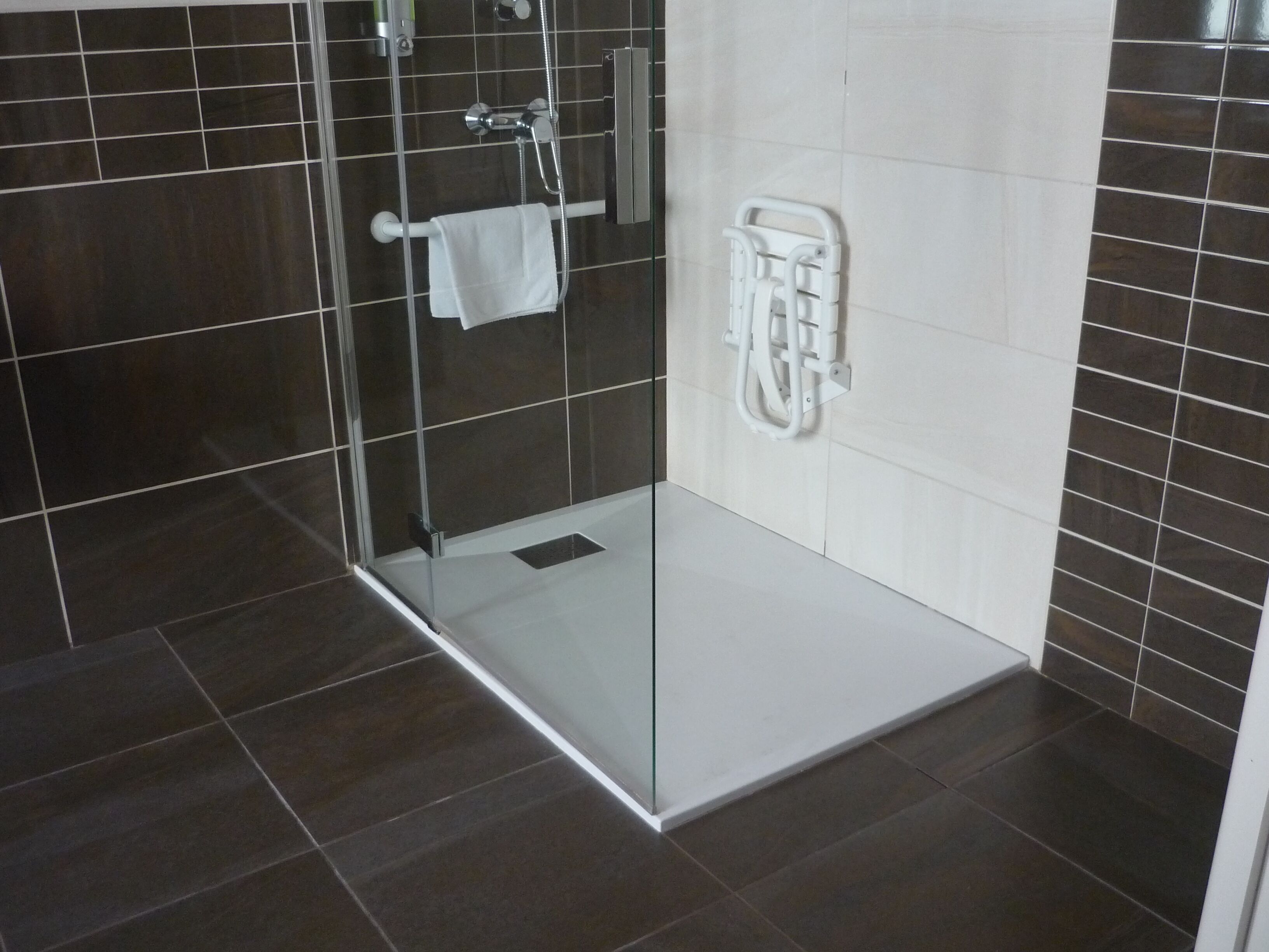 Un baño moderno con cabina de ducha de vidrio, paredes con azulejos blancos y un perchero blanco.