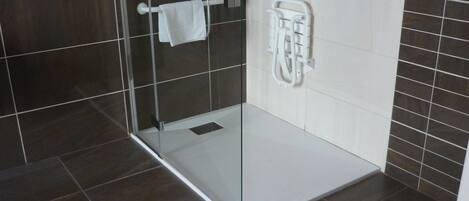 Un baño moderno con cabina de ducha de vidrio, paredes con azulejos blancos y un perchero blanco.