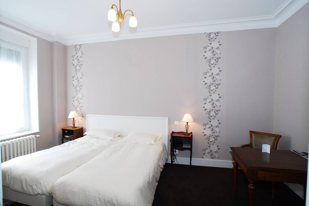 A hotel room with a double bed, two bedside tables with lamps, a wooden chair, and a small table.
