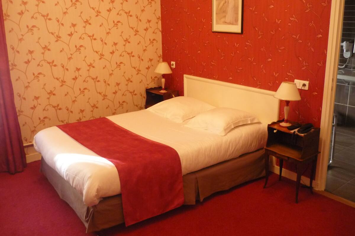 A hotel room with a bed, two bedside tables with lamps, a red carpet, and floral wallpaper.
