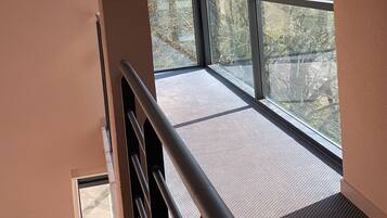 Een trap leidt naar een balkon met grote ramen en uitzicht op bomen en gebouwen.