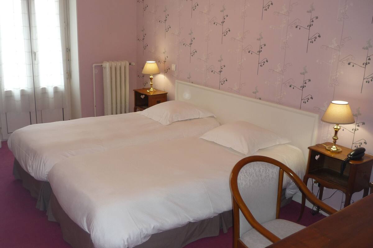A double bed with two bedside tables, each with a lamp, in a room with floral wallpaper and a radiator.