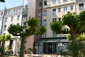 Ein Gebäude mit Glastür, Außenbestuhlung und Bäumen davor.