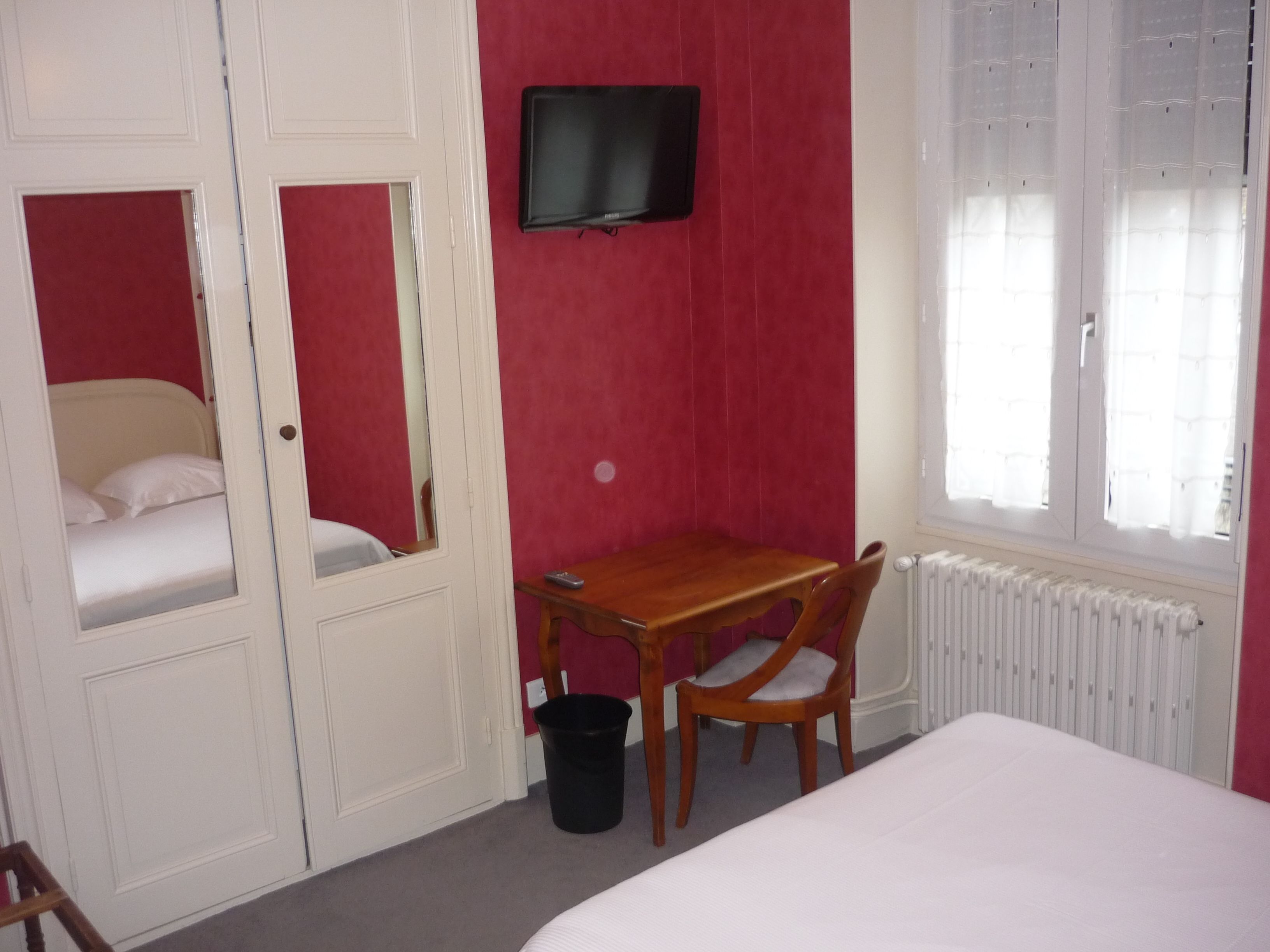 Een kamer met een bed, een bureau, een stoel, een televisie en een radiator.