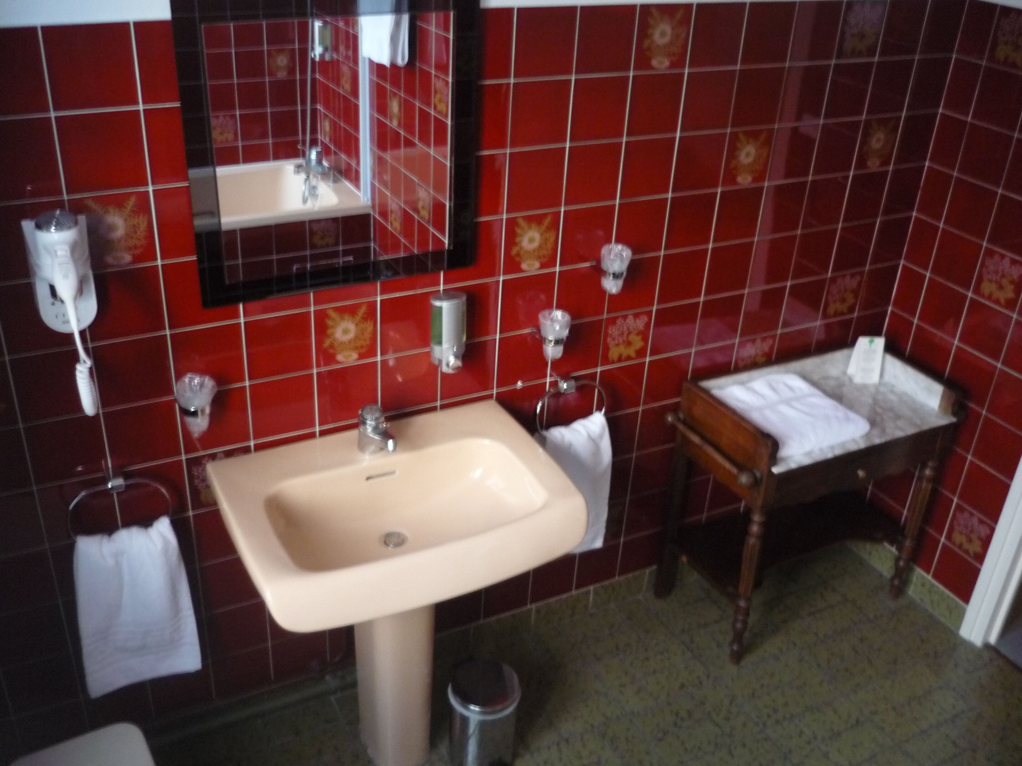 A bathroom with red tiles, a sink, a mirror, and a wooden vanity.