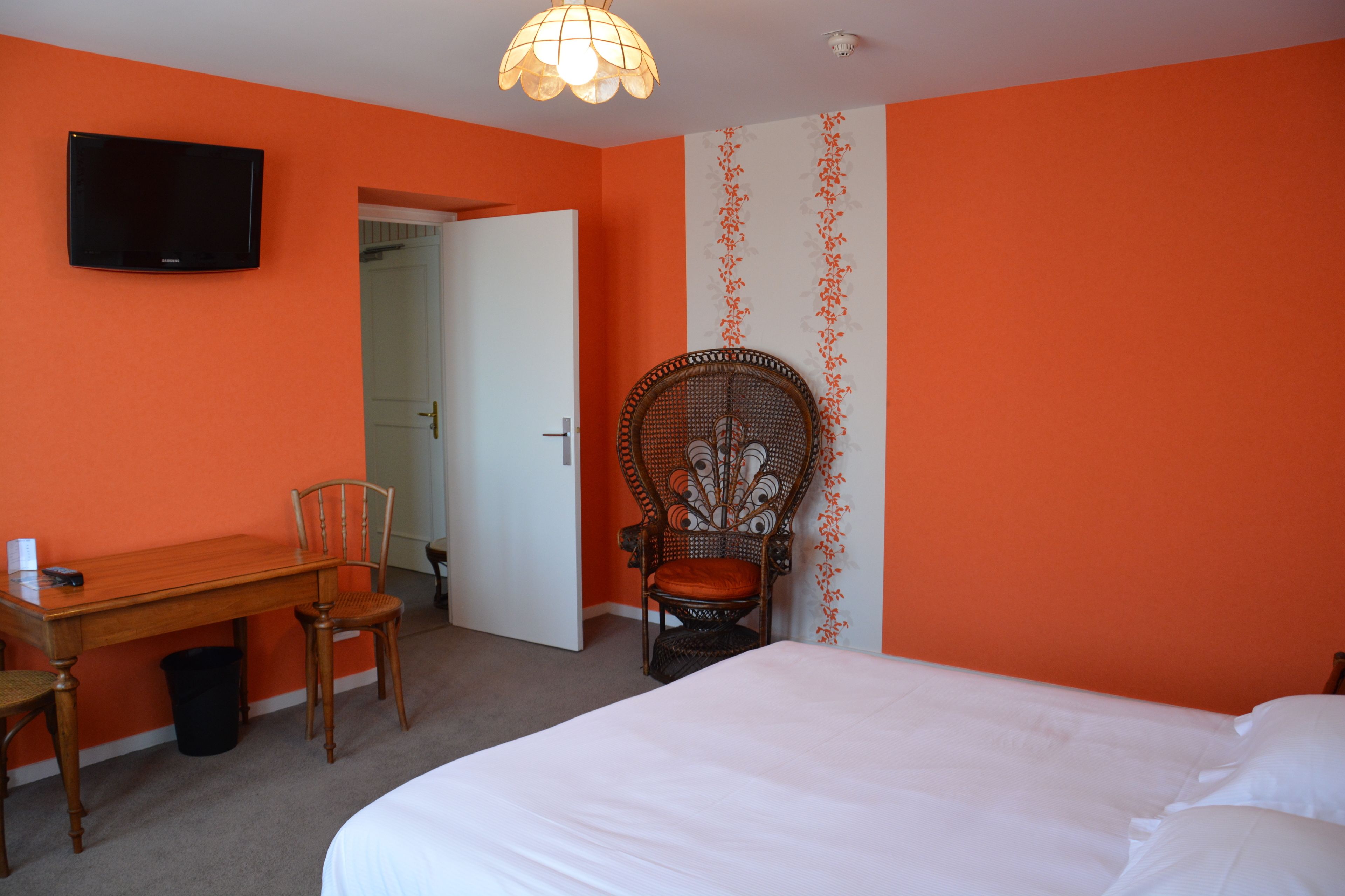 A hotel room with a bed, a desk with a chair, a television mounted on the wall, and a door leading to another room.