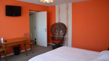 A hotel room with a bed, a desk with a chair, a television mounted on the wall, and a door leading to another room.