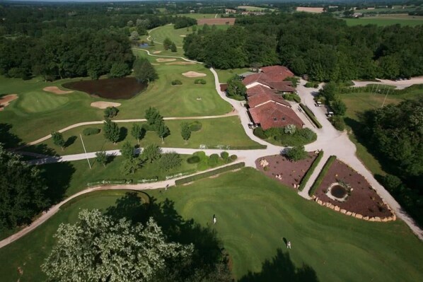 An aerial view of a golf course with a clubhouse, well-maintained fairways, greens, and surrounding wooded areas.