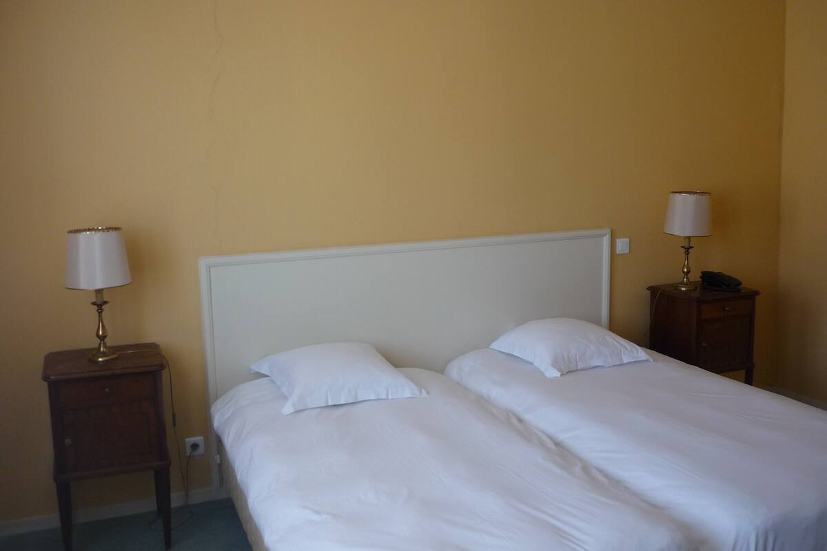 A hotel room with two single beds, a white headboard, and two bedside tables with lamps.