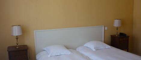 Una habitación de hotel con dos camas individuales, un cabecero blanco y dos mesitas de noche con lámparas.