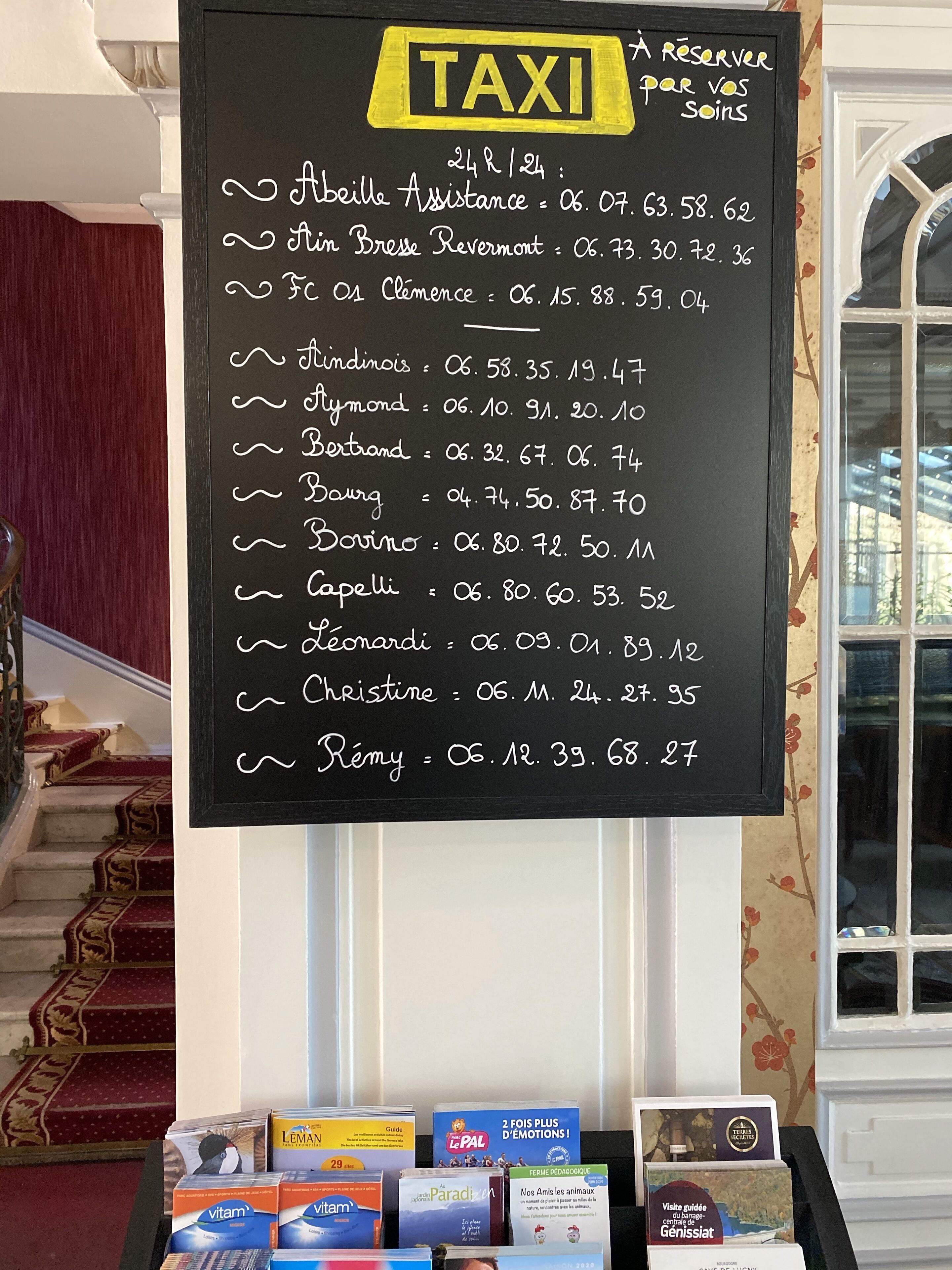 A blackboard with a list of names and times, likely for taxi services, and a display of various health and wellness products below it.
