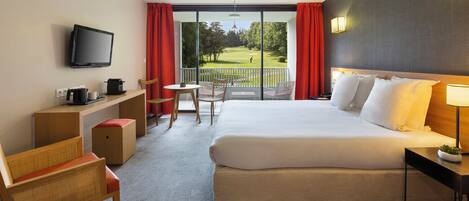 Habitación de hotel con una cama grande, un escritorio con televisor, una silla, una mesita y vistas a un campo de golf por la ventana.