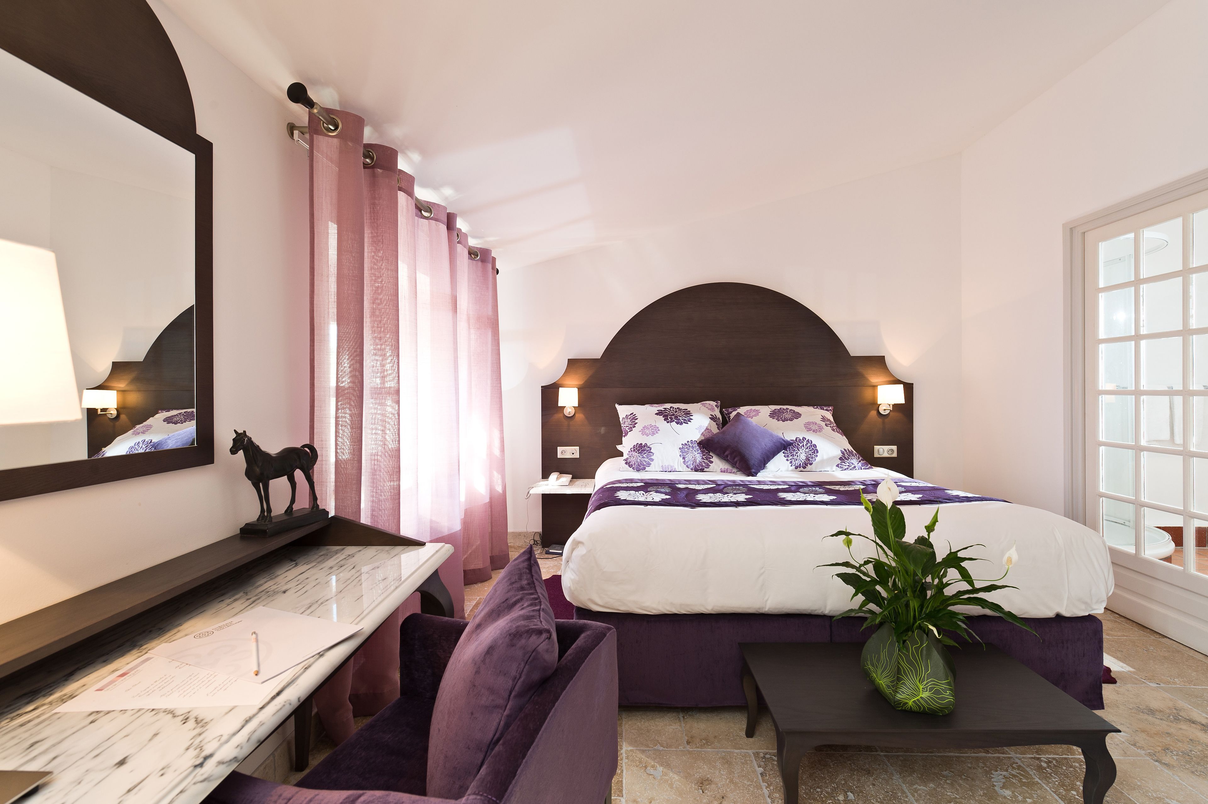 Une chambre à coucher comprenant un lit, un bureau, une chaise, une table de chevet, une lampe, un miroir et une fenêtre.