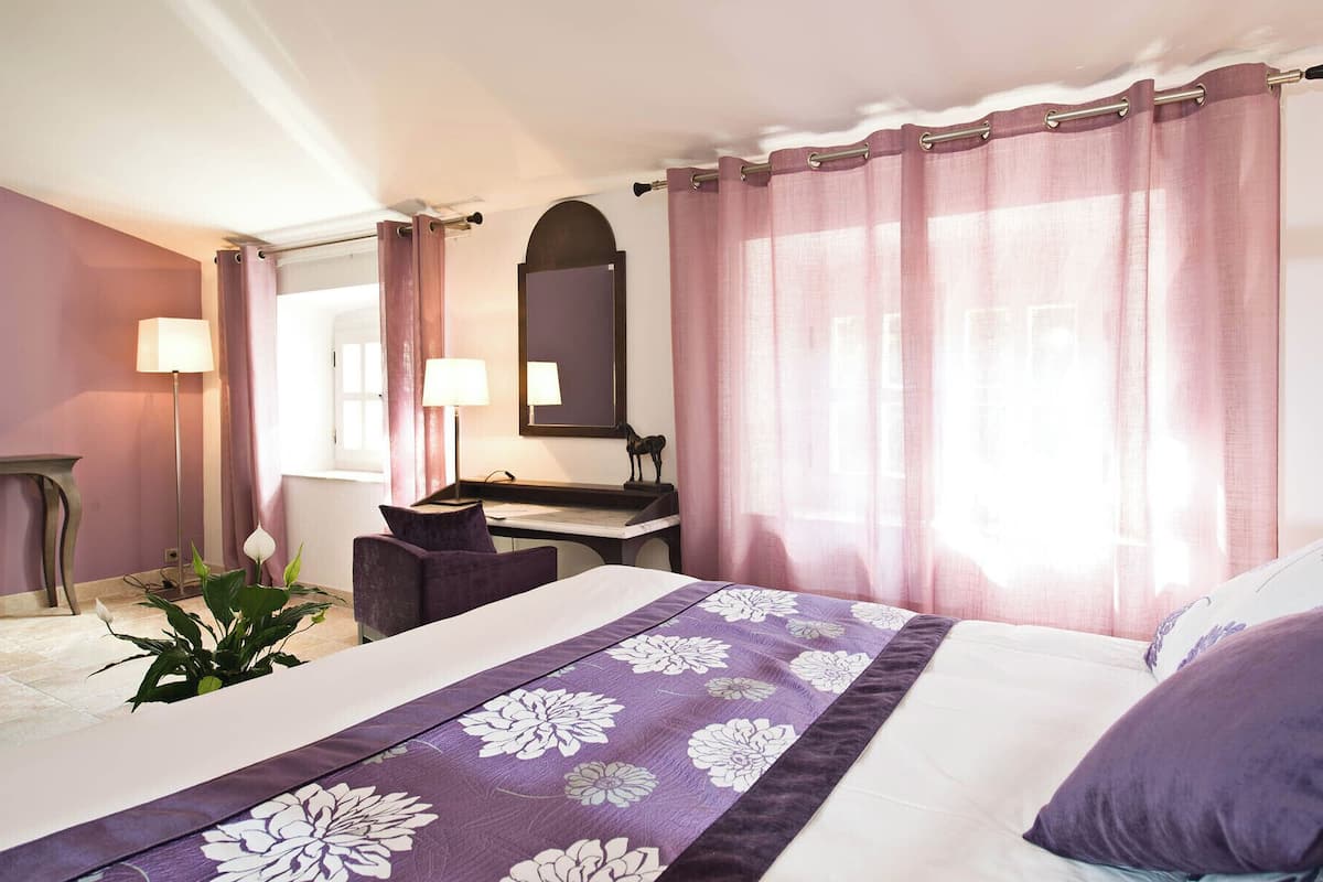 A hotel room with a bed, a desk, a chair, a mirror, and a window with curtains.