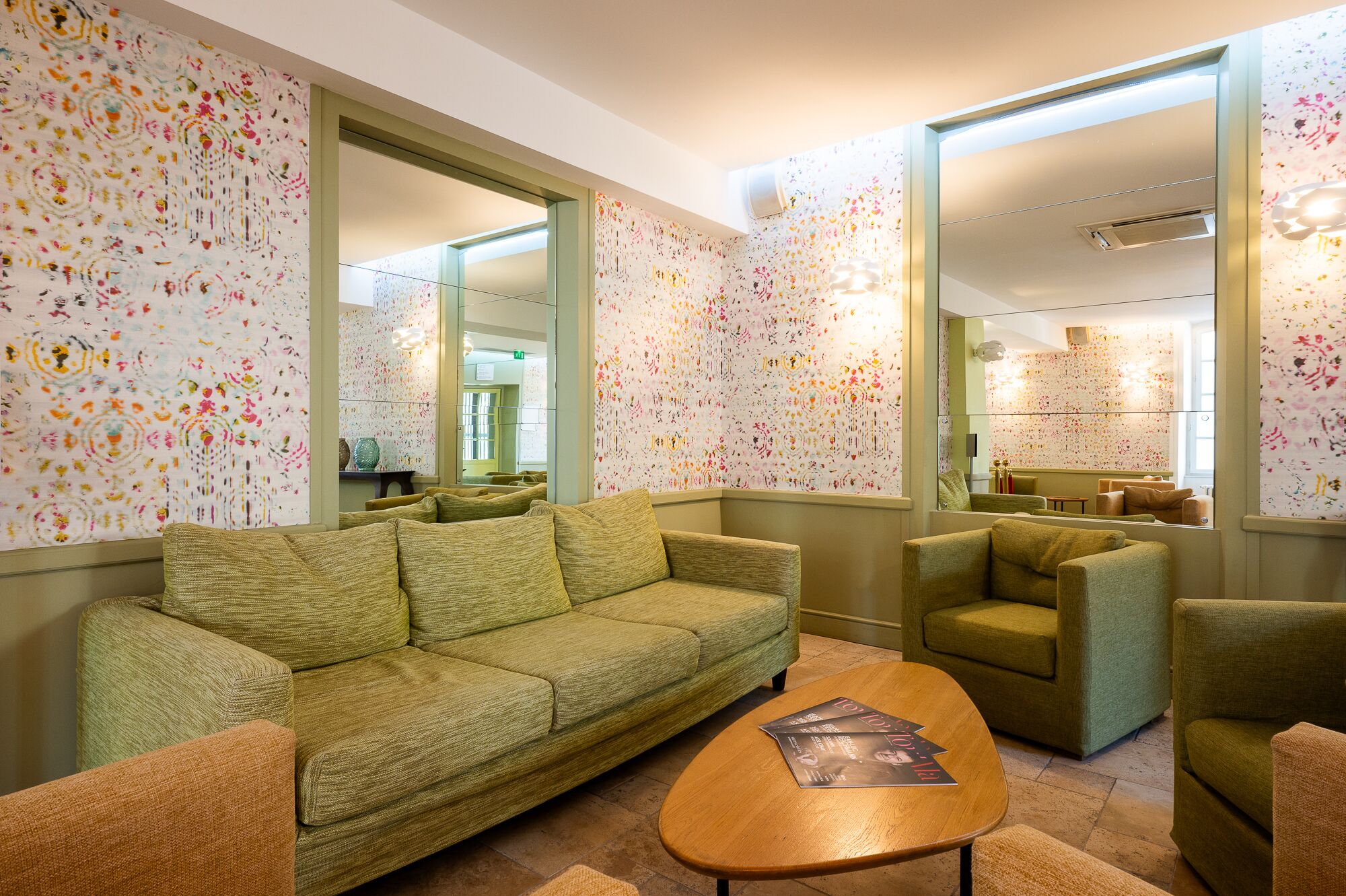 A living room with a green sofa, a wooden coffee table, and a patterned wallpaper.