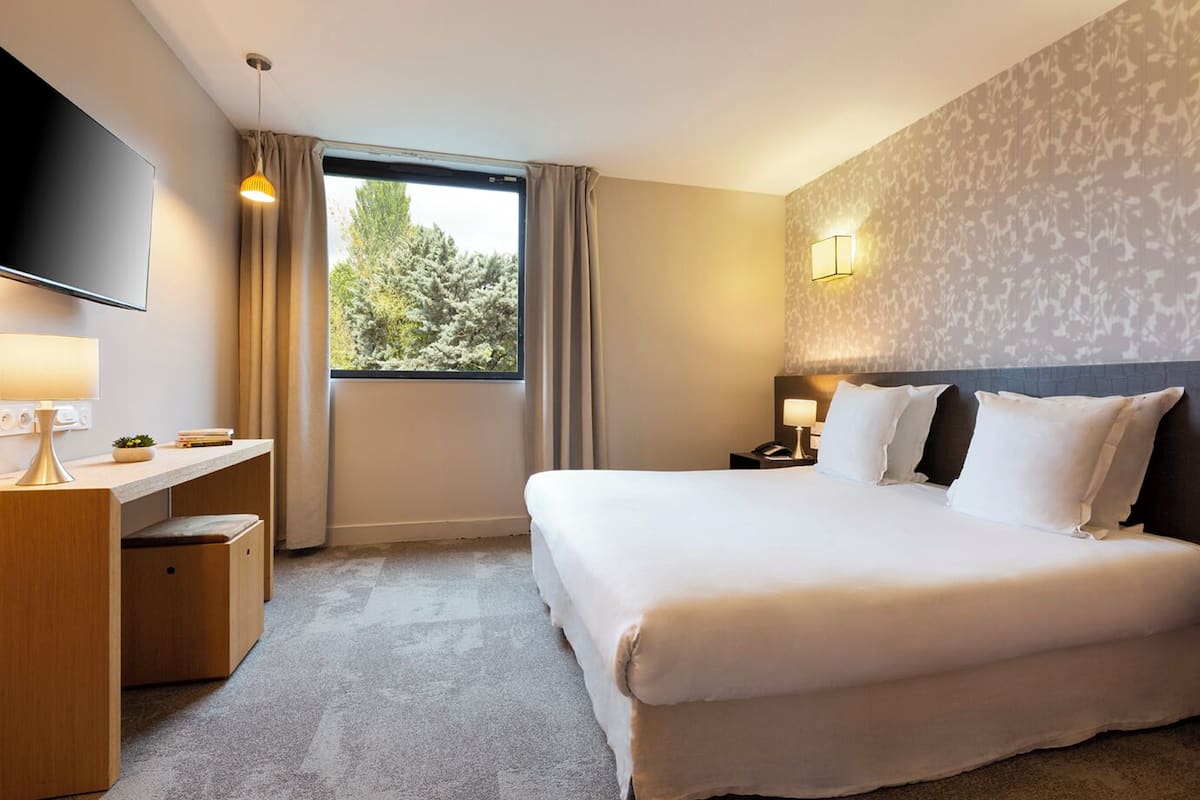 A hotel room with a bed, desk, and TV.