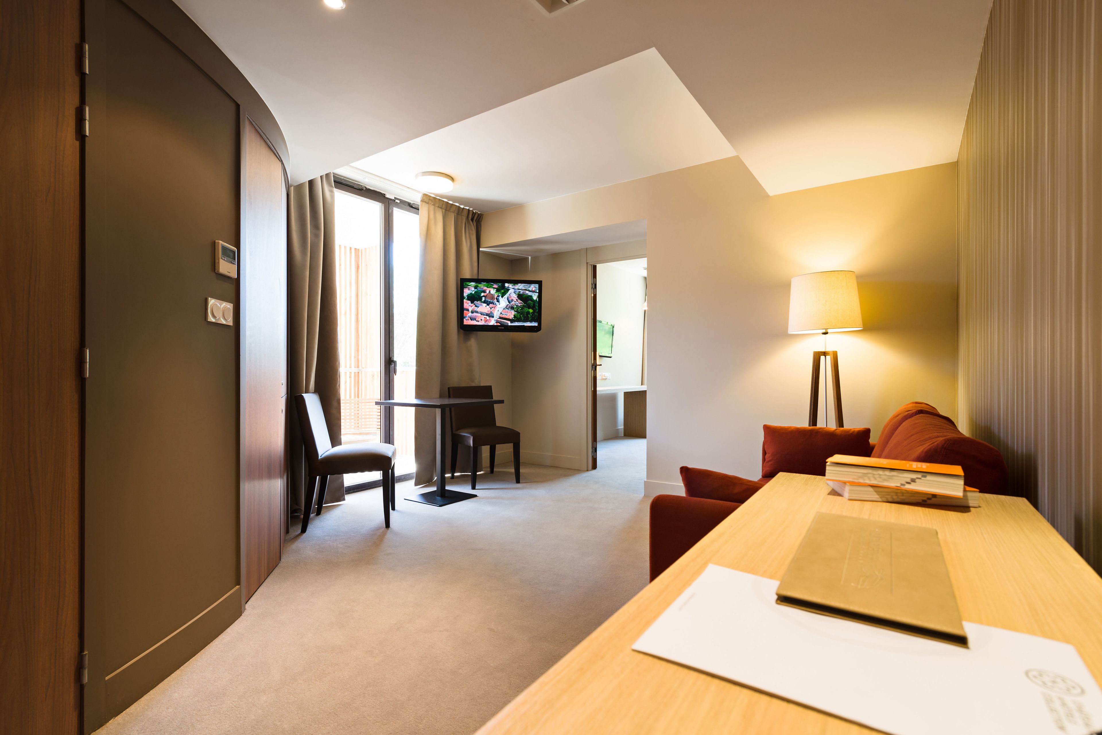 Una habitación de hotel con un escritorio de madera, un televisor, un sofá y una lámpara.