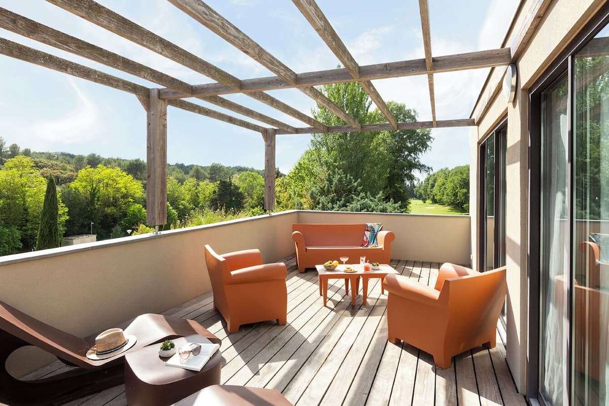 A wooden deck with outdoor furniture, a glass door, and a view of greenery.
