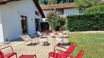 A building with a tiled roof, a door, and a window. There are outdoor chairs and a table.