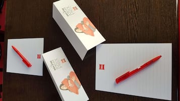 A box of red pens, a lined paper, and a notebook on a wooden surface.
