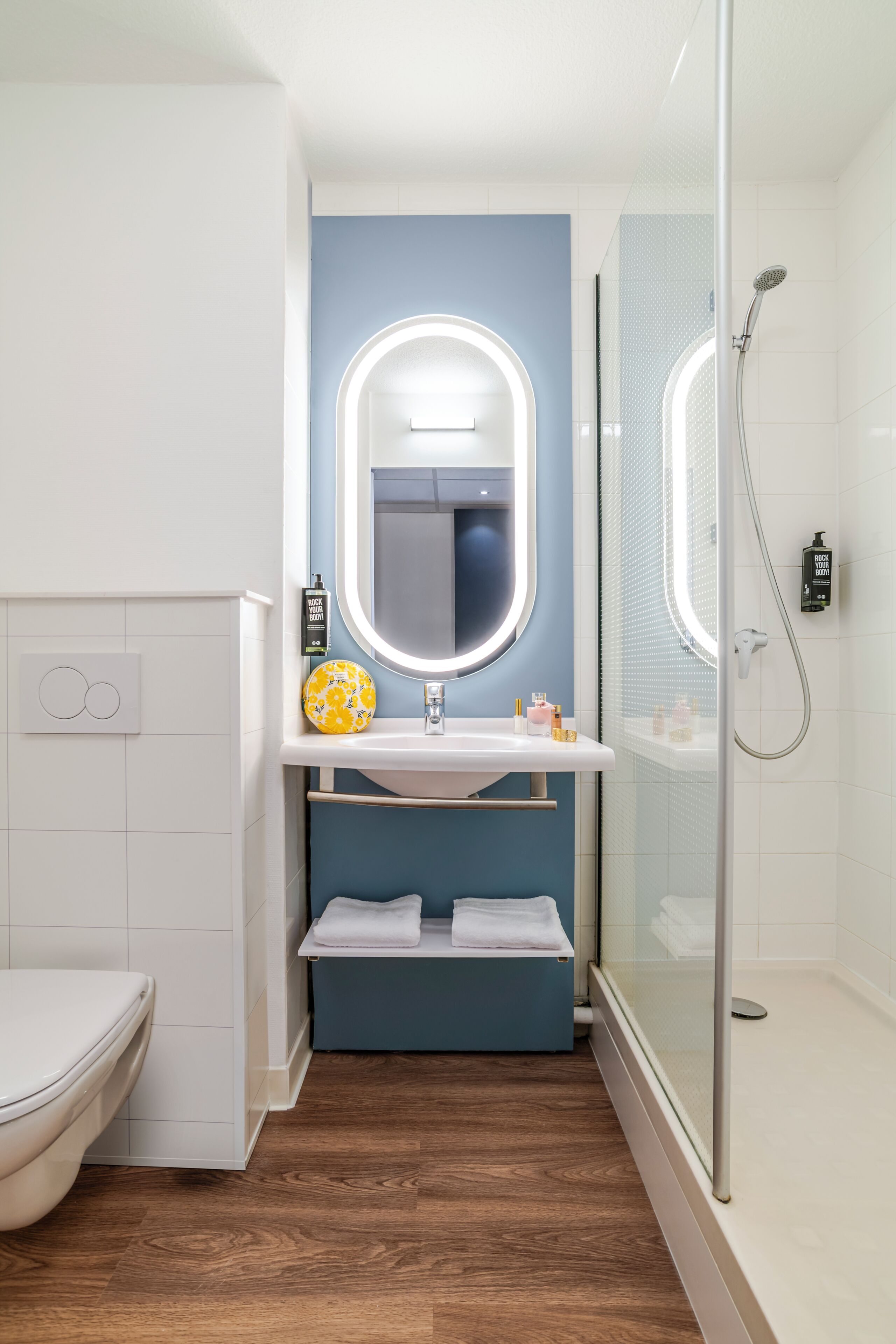 Un baño con inodoro blanco, lavamanos con espejo y zona de ducha.