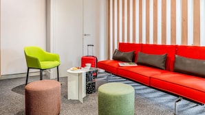 Una habitación de hotel moderna con un sofá rojo, una silla verde y una mesita con una maleta roja.