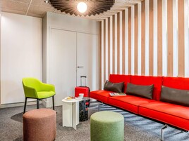 Una habitación de hotel moderna con un sofá rojo, una silla verde y una mesita con una maleta roja.