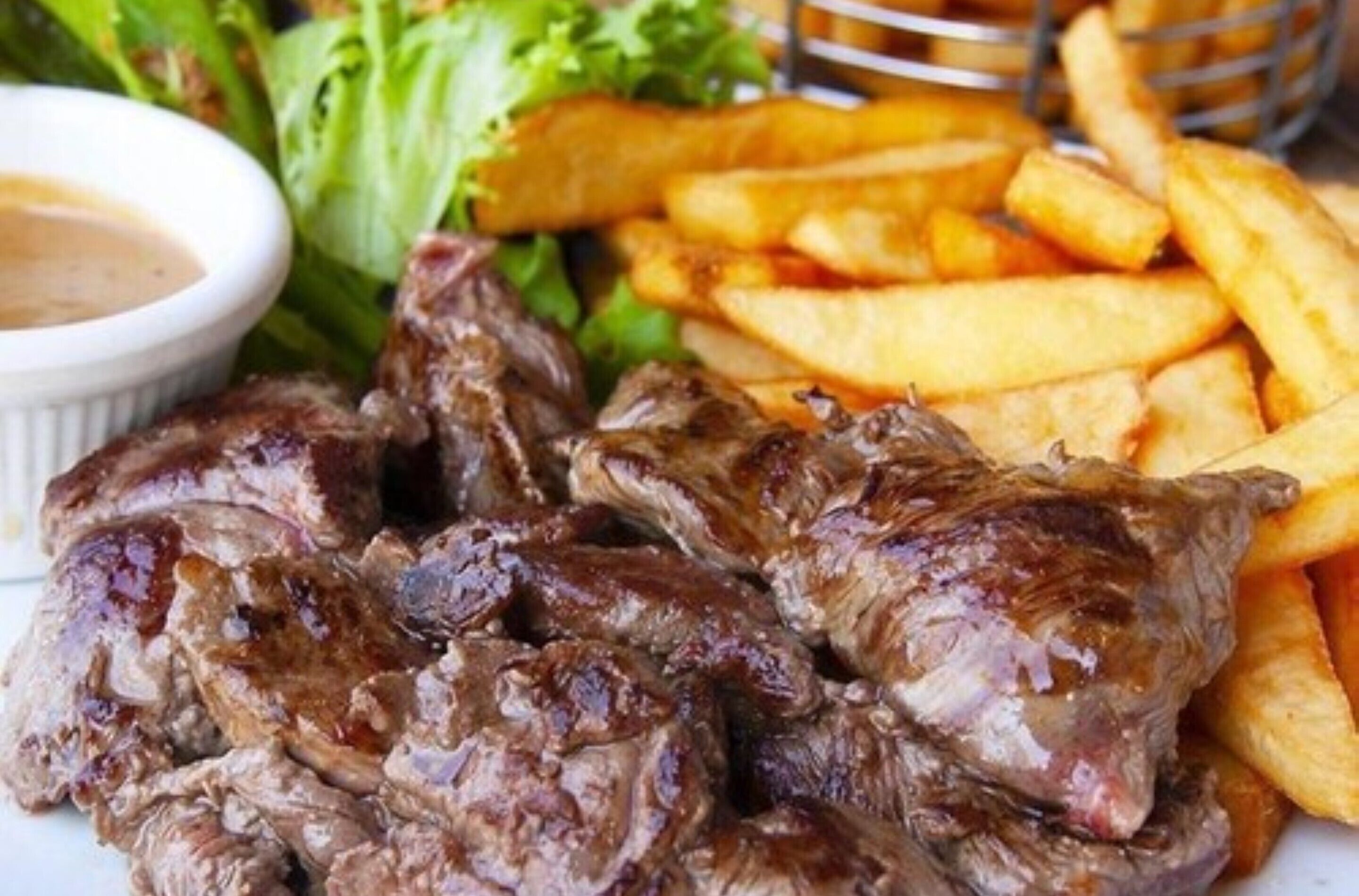 A plate of grilled meat and French fries with a side of salad and dipping sauce.