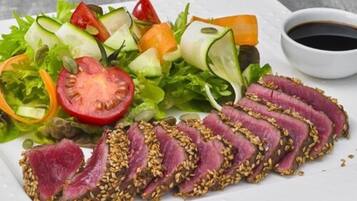 A plate with sliced meat topped with sesame seeds, a mixed vegetable salad, and a small bowl of sauce.