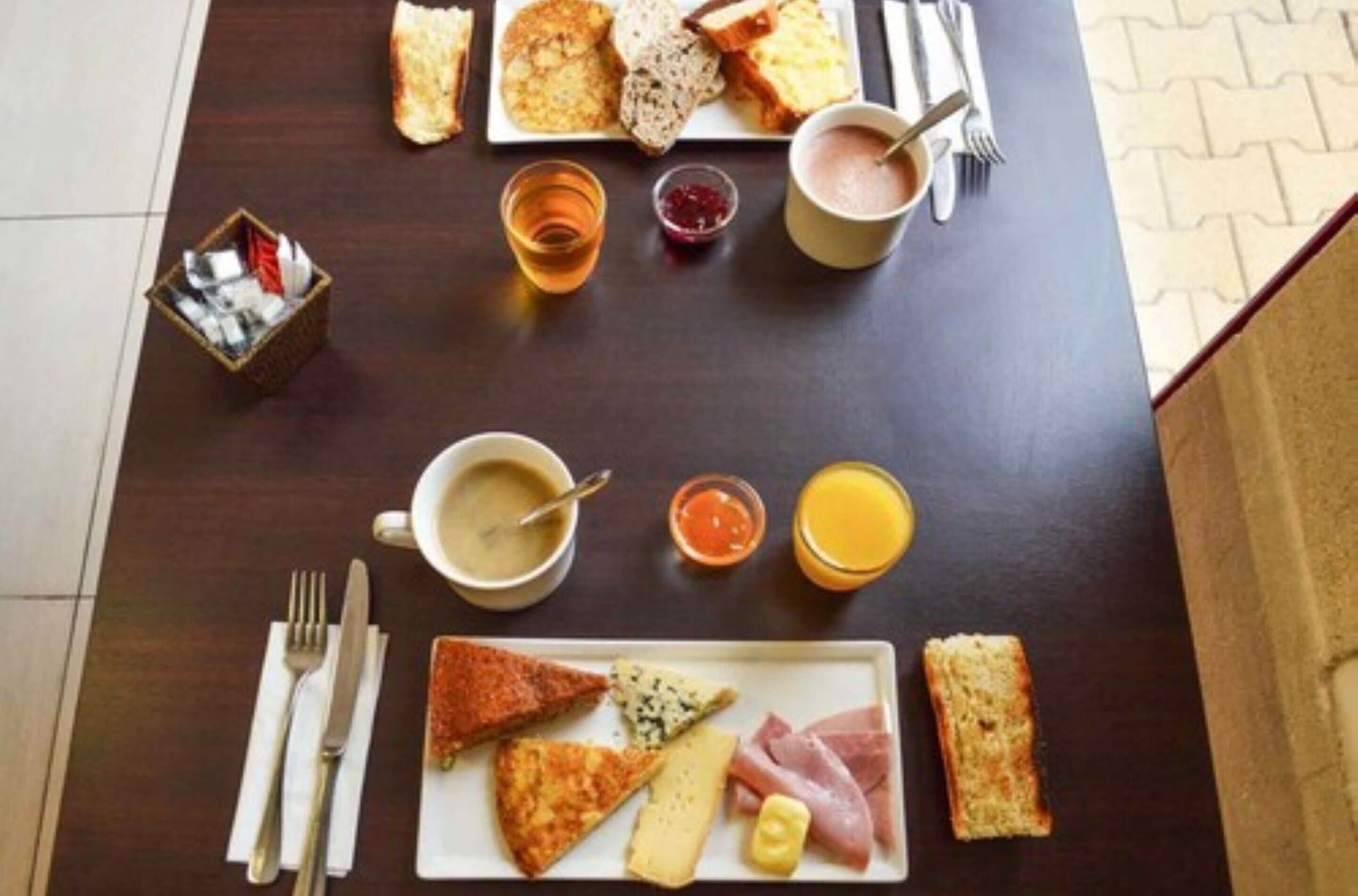 A breakfast setting with toast, eggs, cheese, ham, and beverages on a table.