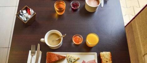 Una mesa con desayuno: tostadas, huevos, queso, jamón y bebidas.