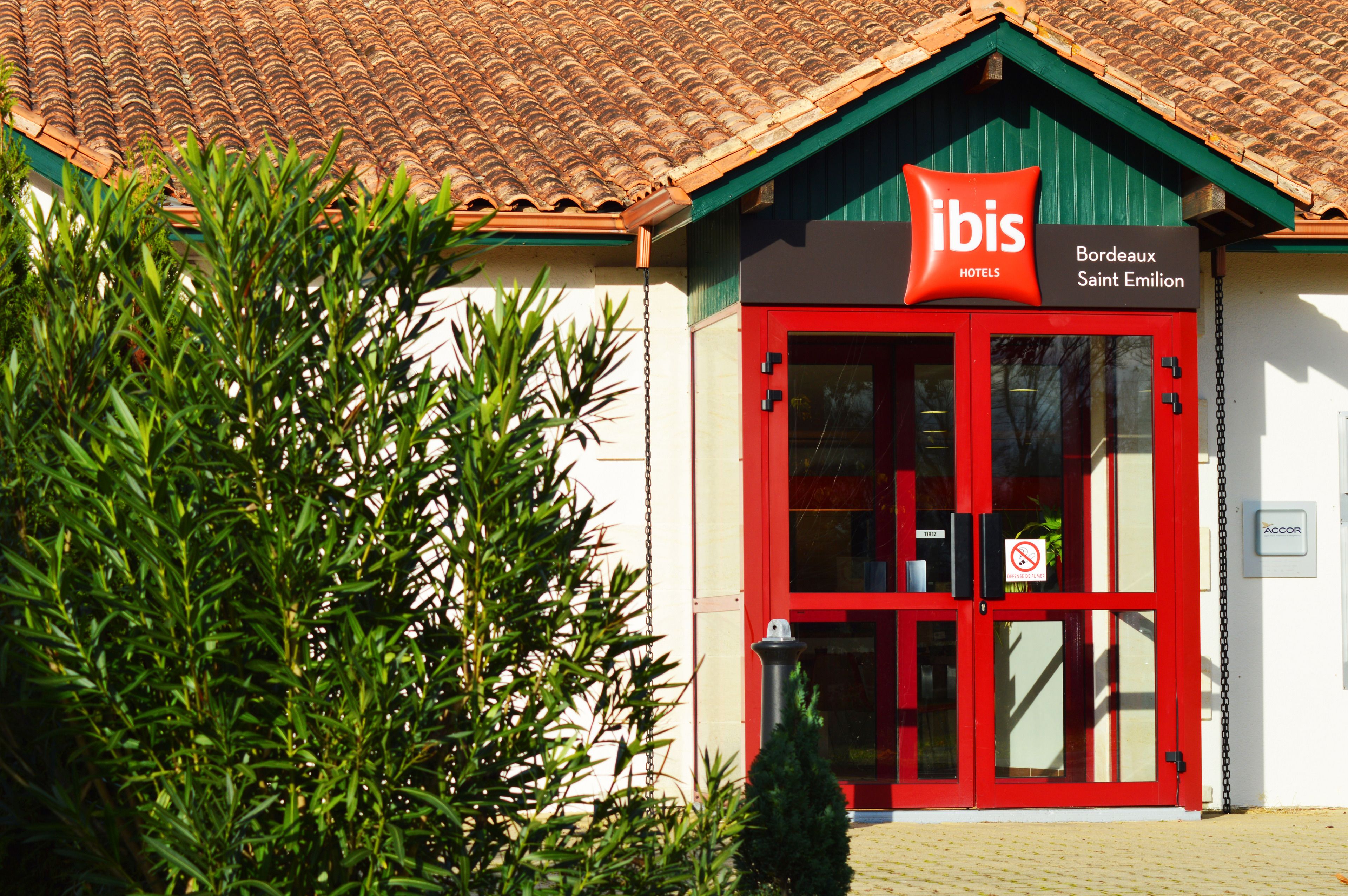 A hotel entrance with a red door, a sign reading "ibis Hotels Bordeaux Saint Emilian", and a no-smoking sign.