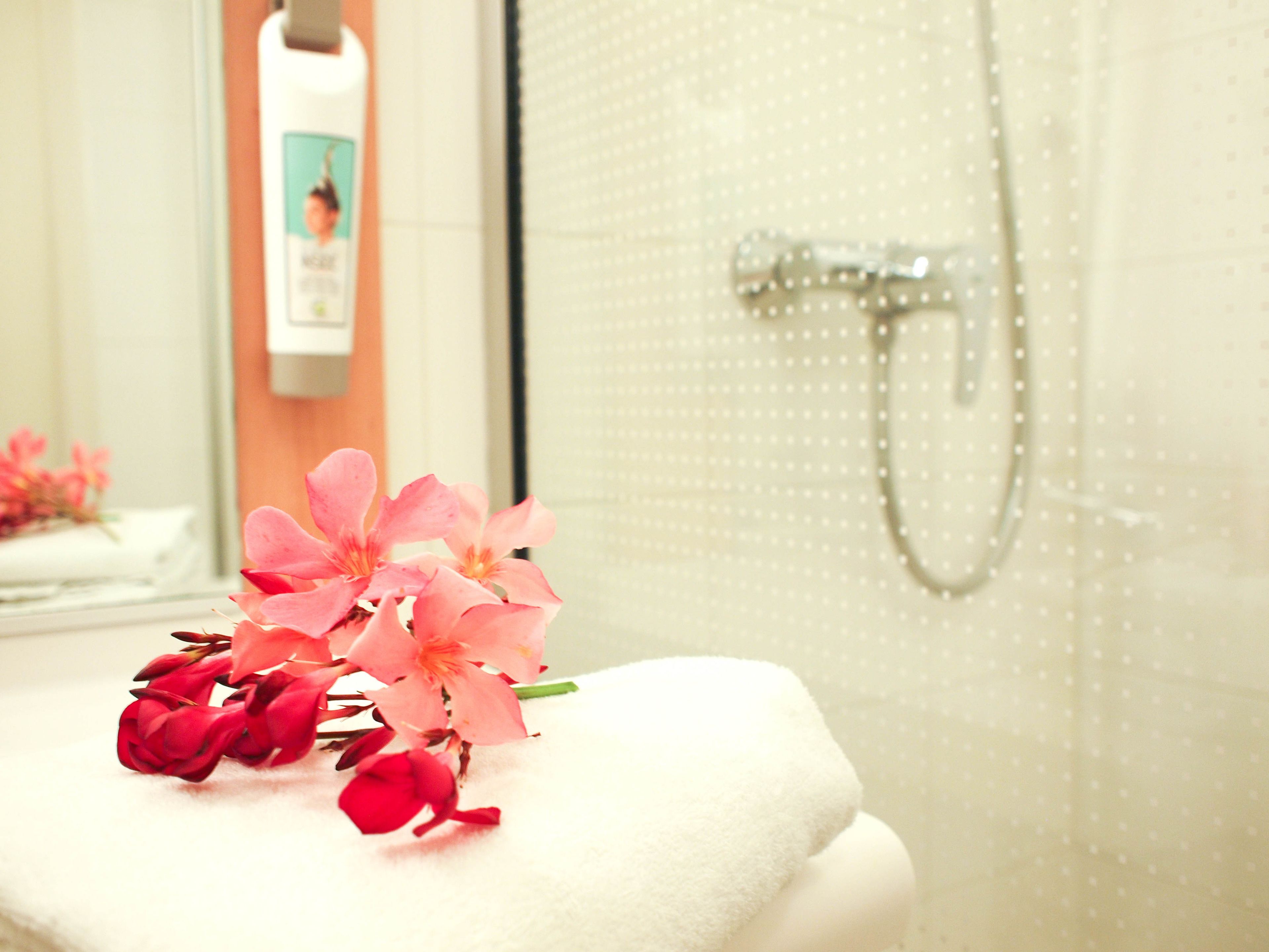 A bathroom with a white towel, pink flowers, and a shower.