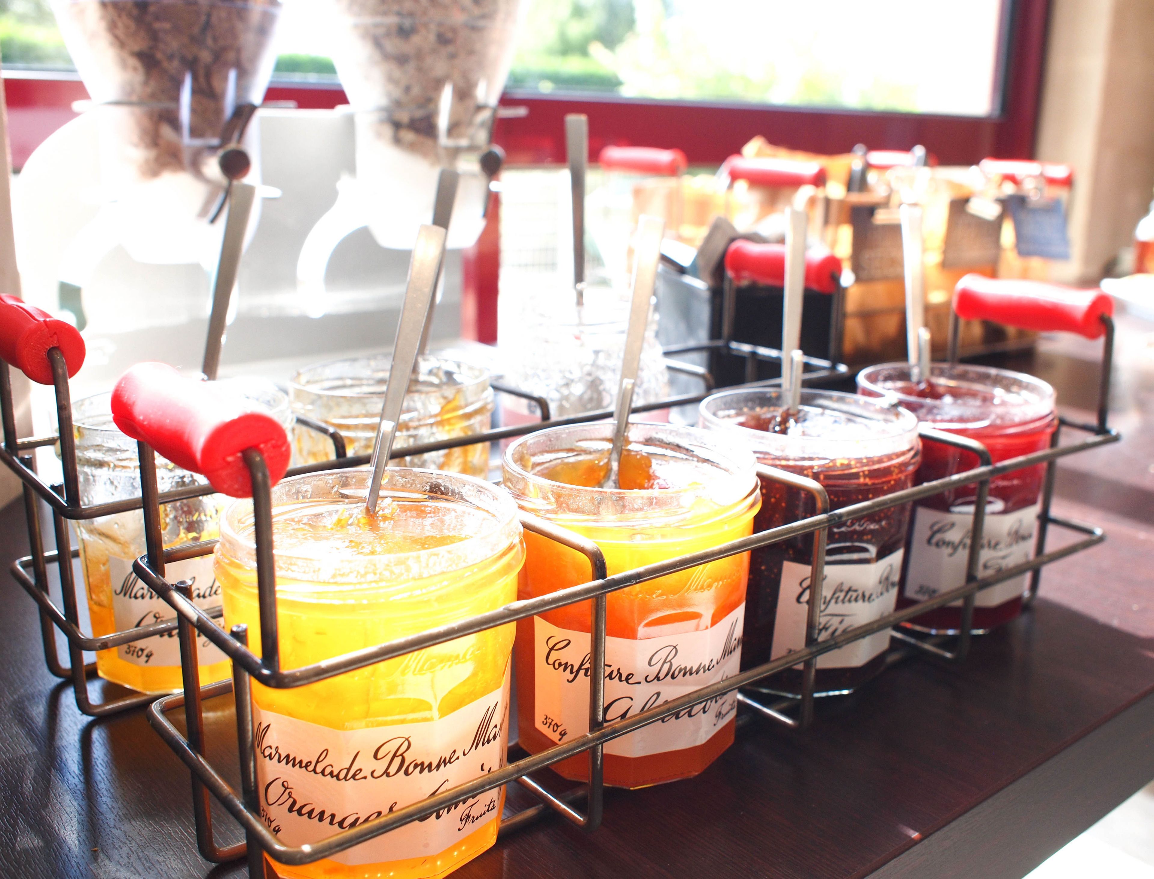 A display of jars with labels, some with red handles, on a metal rack.