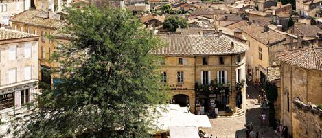 A town square with stone paving, historic buildings, and a large tree.