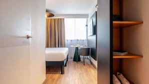 Habitación de hotel con cama, escritorio, silla, televisor y estante para zapatos.