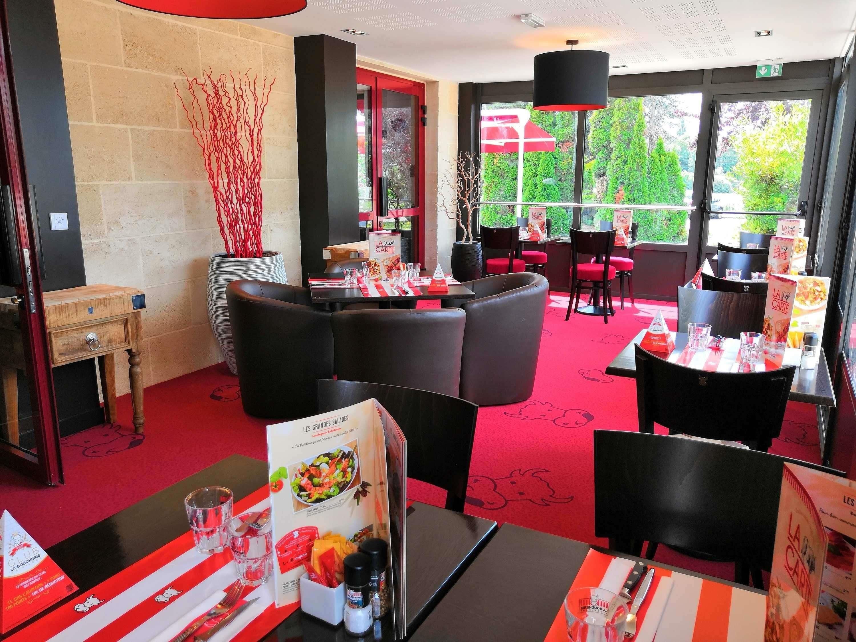 Un restaurante con decoración en rojo y negro, mesas con menús y vistas al exterior con vegetación.