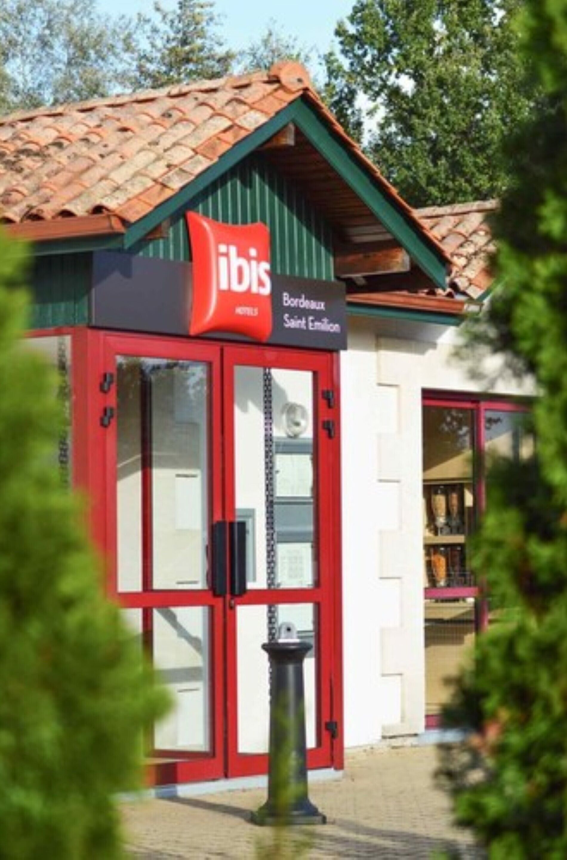 Un edificio con fachada roja y blanca, un letrero que dice "ibis Bordeaux Saint Emilian" y techo de tejas.