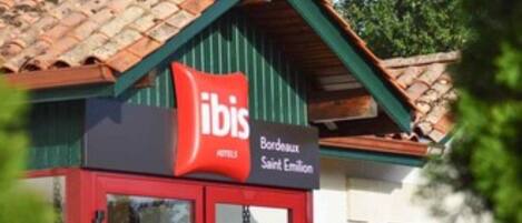 Un edificio con fachada roja y blanca, un letrero que dice "ibis Bordeaux Saint Emilian" y techo de tejas.