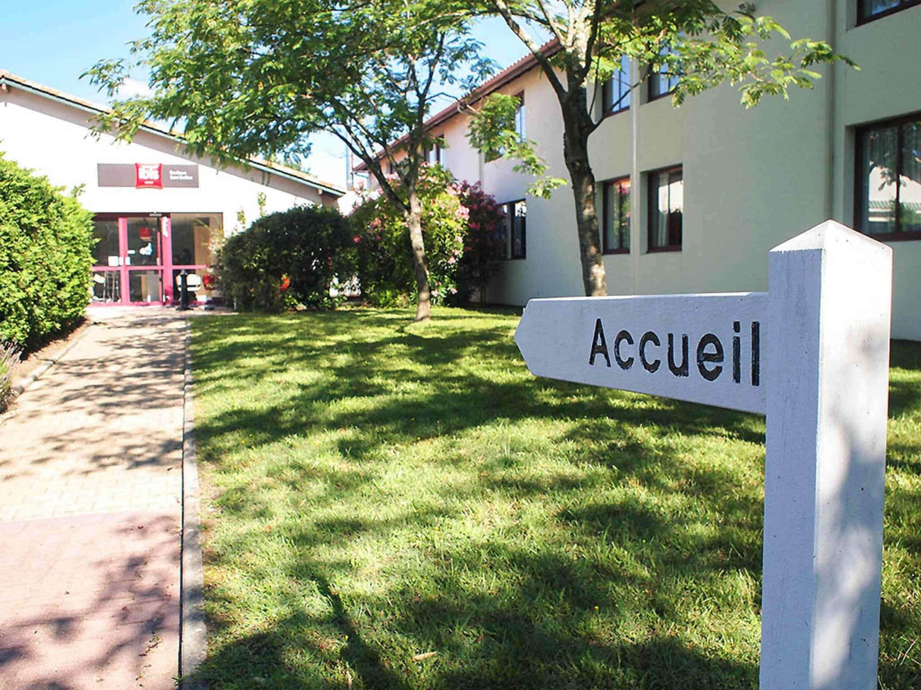 A signpost with 'Accueil' indicating the entrance to a building, surrounded by a well-maintained lawn and trees.